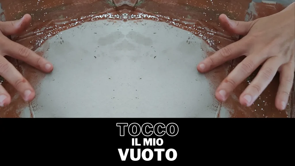 Primo piano di una mano che tocca una superficie scura e bagnata, con la scritta in basso 'TOCCO IL MIO VUOTO'. Immagine relativa all'esplorazione emotiva in un laboratorio di arteterapia.
