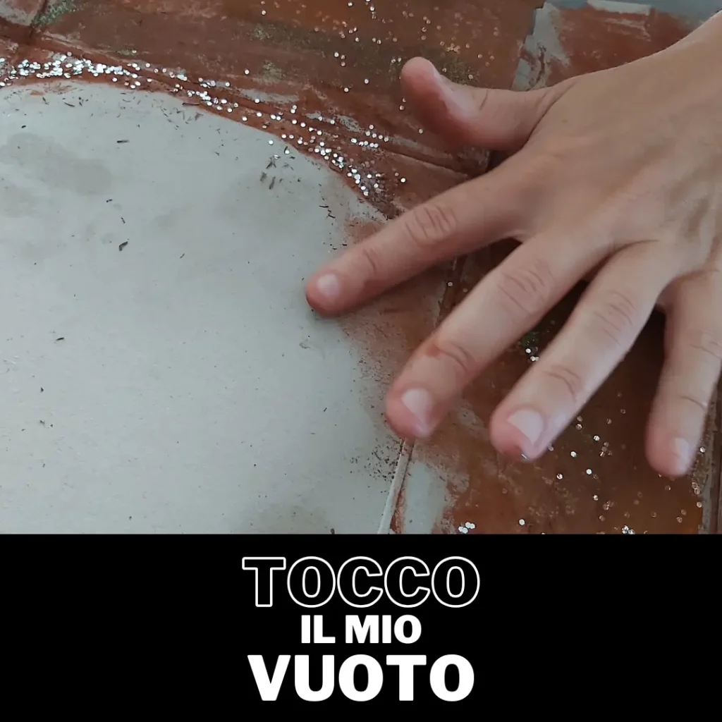 Primo piano di una mano che tocca una superficie scura e bagnata, con la scritta in basso 'TOCCO IL MIO VUOTO'. Immagine relativa all'esplorazione emotiva in un laboratorio di arteterapia.